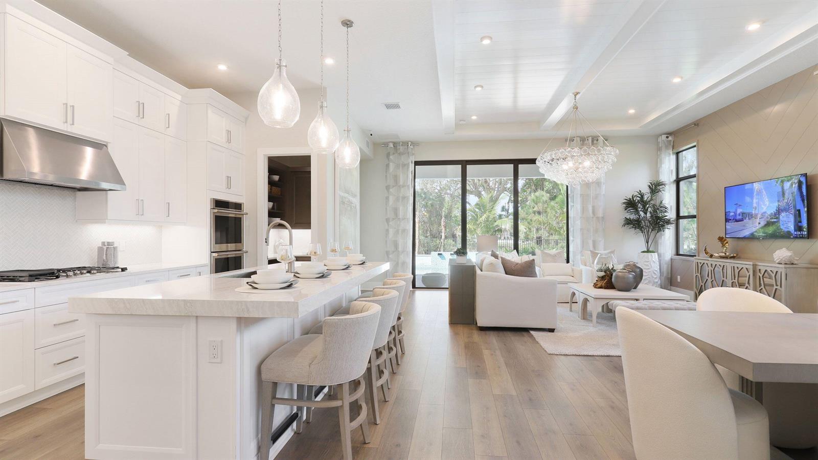 A bright open-concept kitchen and living area featuring white cabinetry, a large island, and flooring — 1891 SE Royale Preserve Way, Stuart FL 34997, STUART, FL