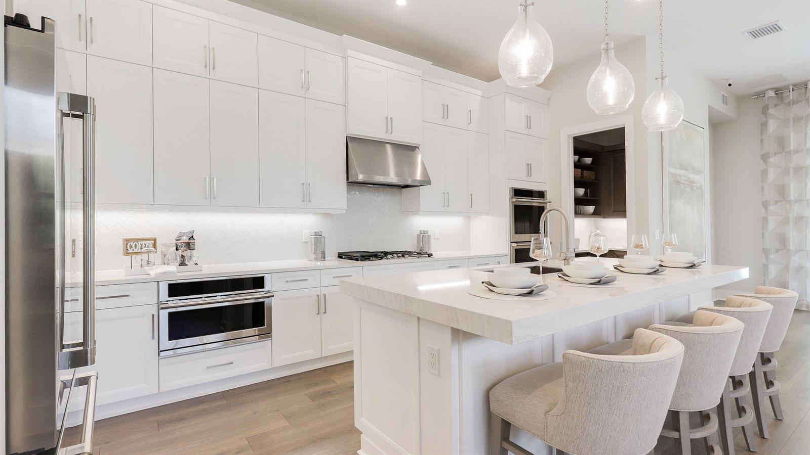 A modern white kitchen features a large island with bar seating and stainless steel appliances — 1891 SE Royale Preserve Way, Stuart FL 34997, STUART, FL