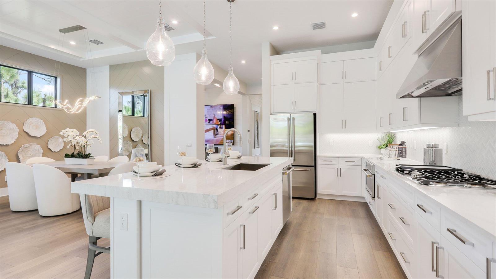 A modern kitchen features white cabinetry, a marble-topped island, and an adjacent dining area — 1891 SE Royale Preserve Way, Stuart FL 34997, STUART, FL