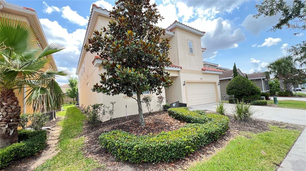 A two-story stucco house features a front yard with a large tree and manicured hedges — 6041 BROAD OAK DRIVE, DAVENPORT, FL