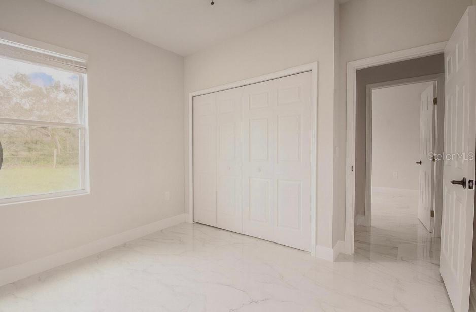 An empty bedroom features white walls, a white closet, and light-colored marble-look tile flooring — 603 AMAZON PLACE, KISSIMMEE, FL
