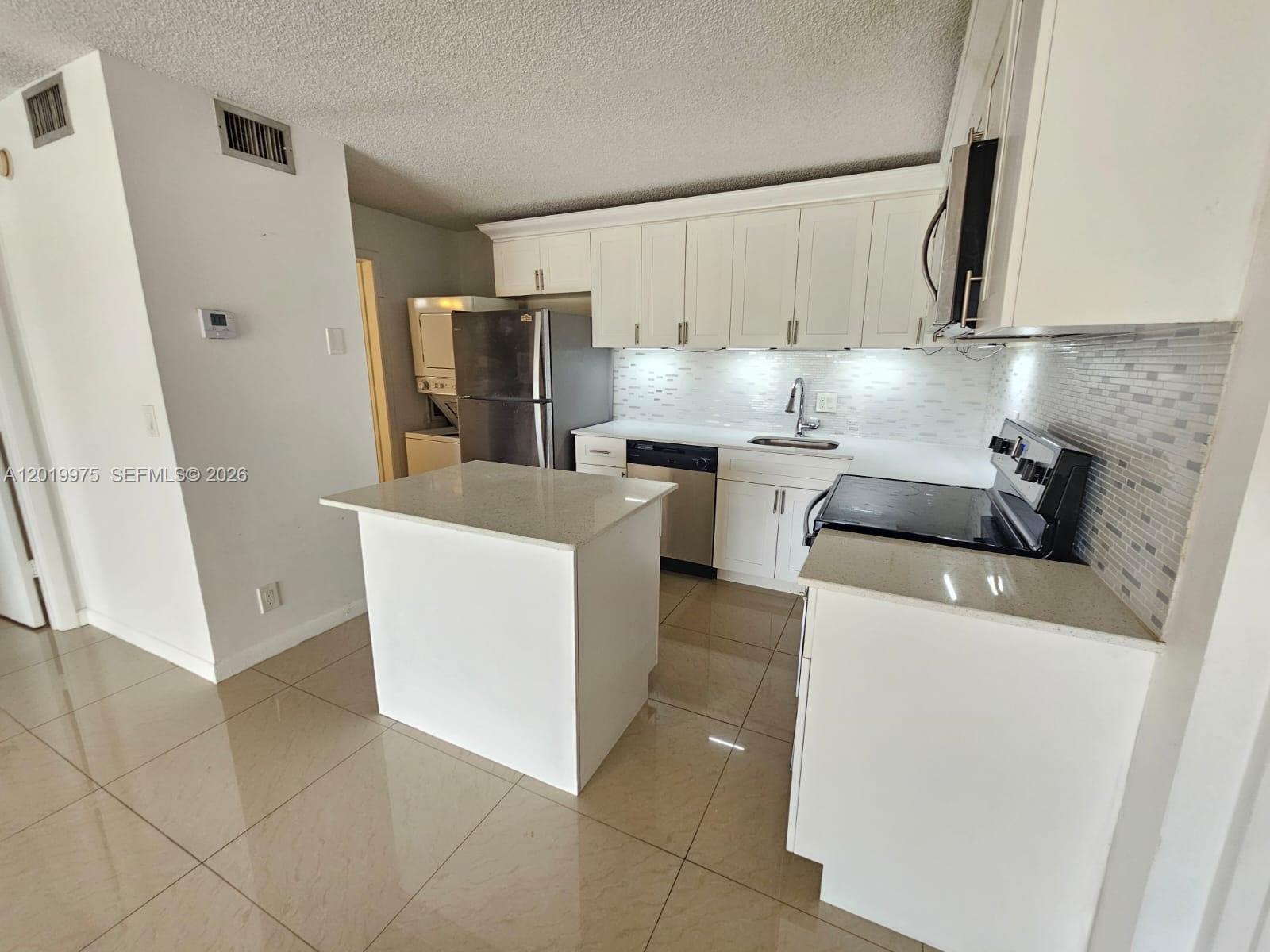 A kitchen features white cabinets, stainless steel appliances, a center island, and tiled flooring — 1105 Green Pine Blvd # E3, West Palm Beach FL 33409, WEST PALM BEACH, FL