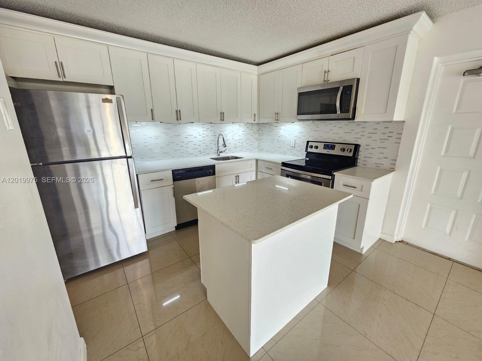 A kitchen features white cabinets, stainless steel appliances, a center island, and tiled flooring — 1105 Green Pine Blvd # E3, West Palm Beach FL 33409, WEST PALM BEACH, FL
