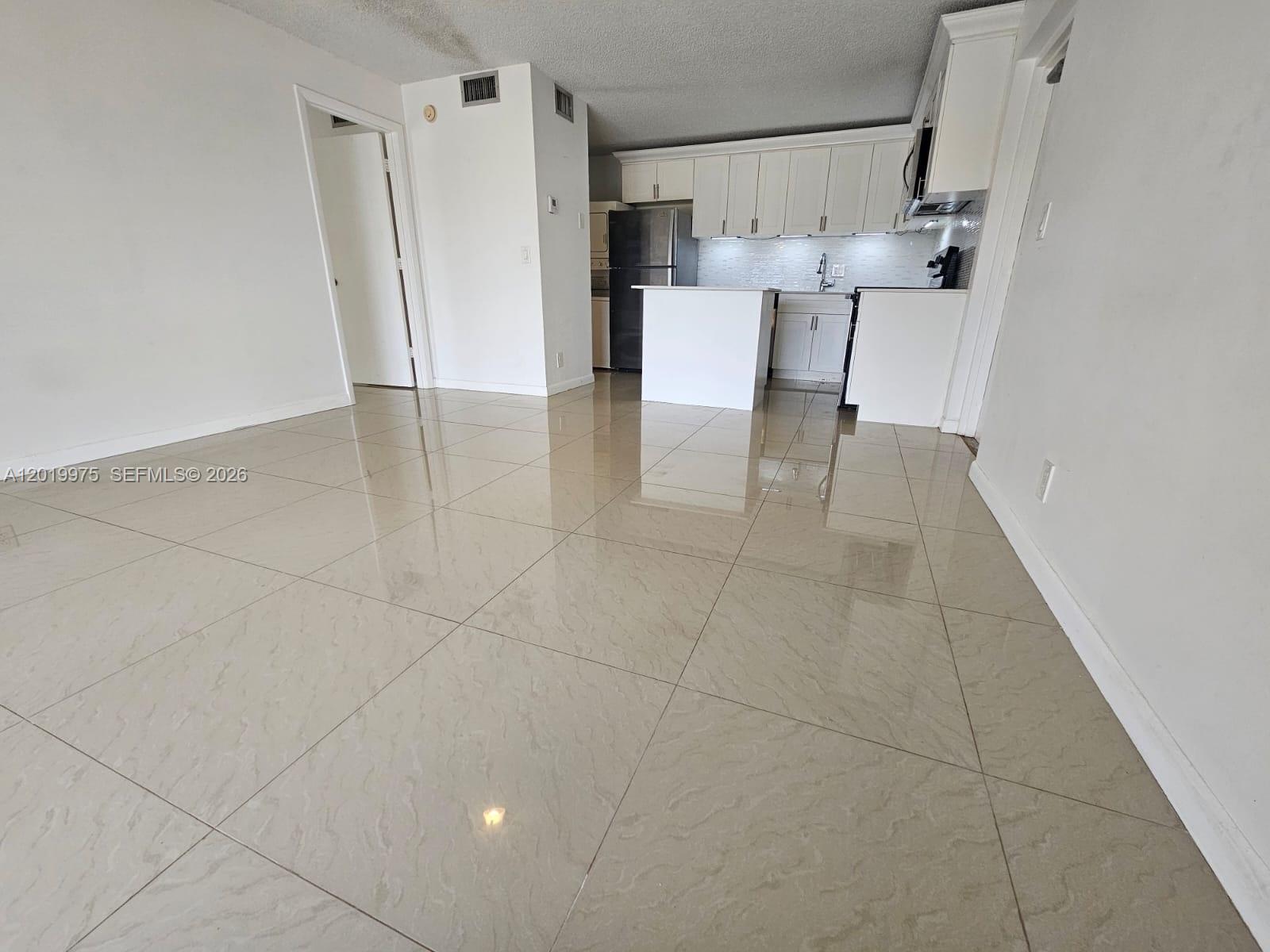 A kitchen with white cabinets and a small island overlooks a tiled living area — 1105 Green Pine Blvd # E3, West Palm Beach FL 33409, WEST PALM BEACH, FL