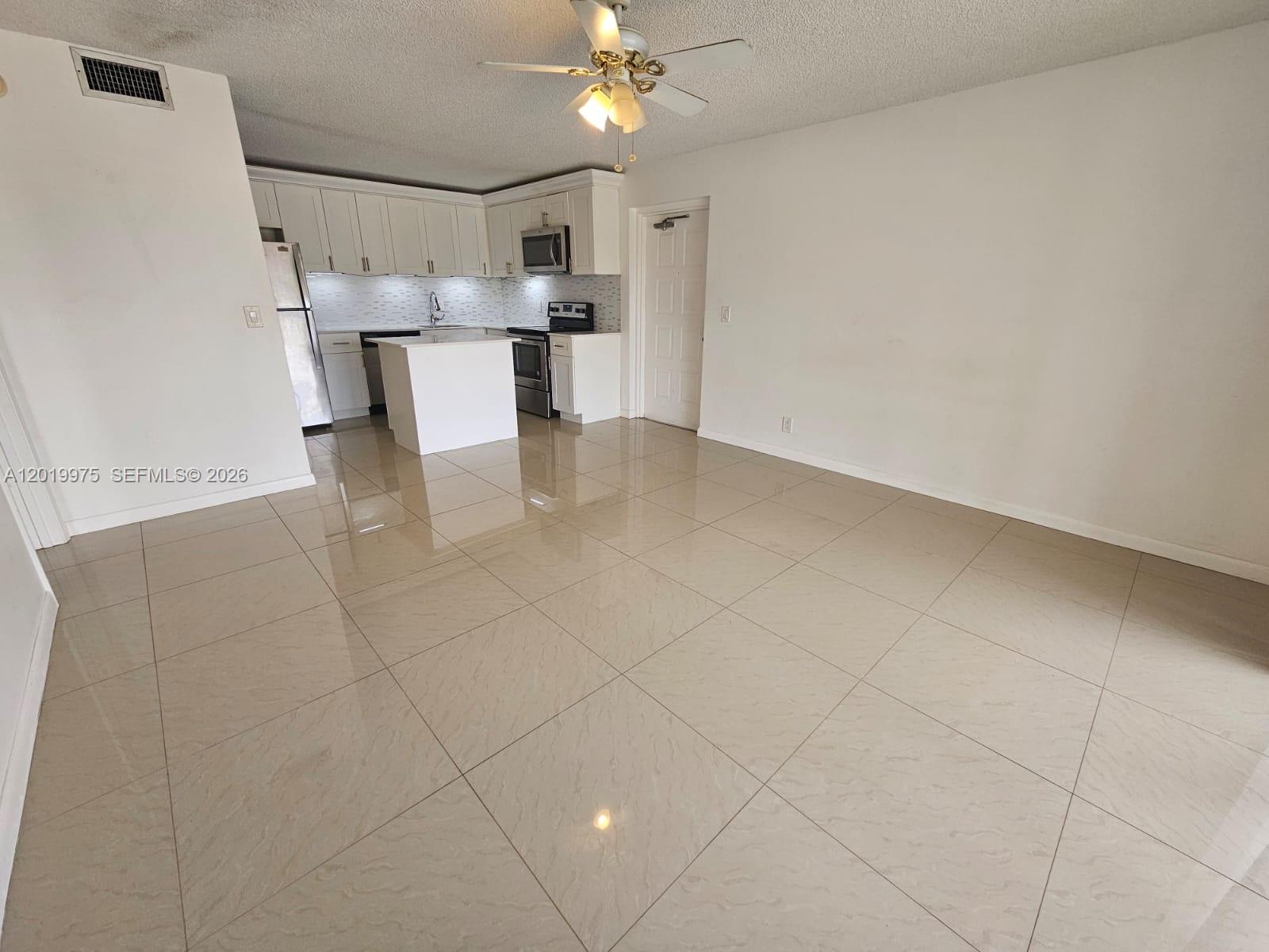 An open-concept kitchen with white cabinets and a center island overlooks a tiled living area — 1105 Green Pine Blvd # E3, West Palm Beach FL 33409, WEST PALM BEACH, FL