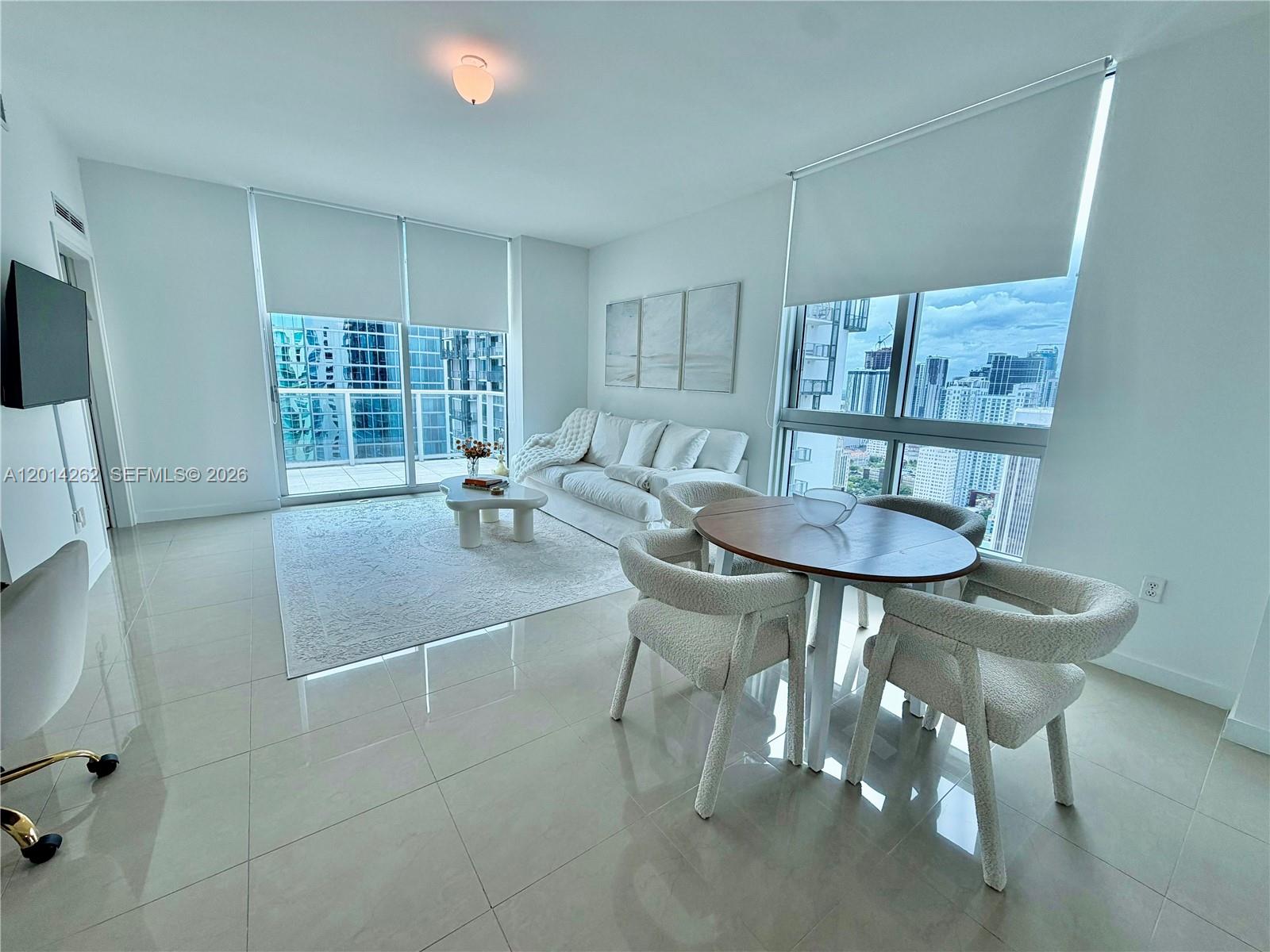 A modern living and dining area features white tile floors, floor-to-ceiling windows, and city views — 300 S Biscayne Blvd # 3701, Miami FL 33131, MIAMI, FL