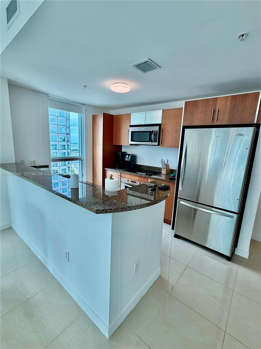 A kitchen features wood cabinets, stainless steel appliances, and a curved granite breakfast bar — 300 S Biscayne Blvd # 3701, Miami FL 33131, MIAMI, FL