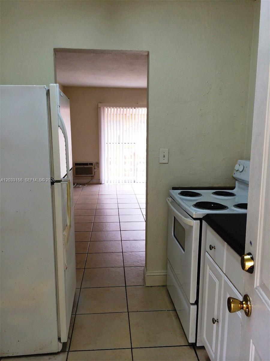 A narrow kitchen with white appliances and tile flooring leads into an adjacent living area — 2441 NW 13 ST # 77, Miami FL 33125, MIAMI, FL