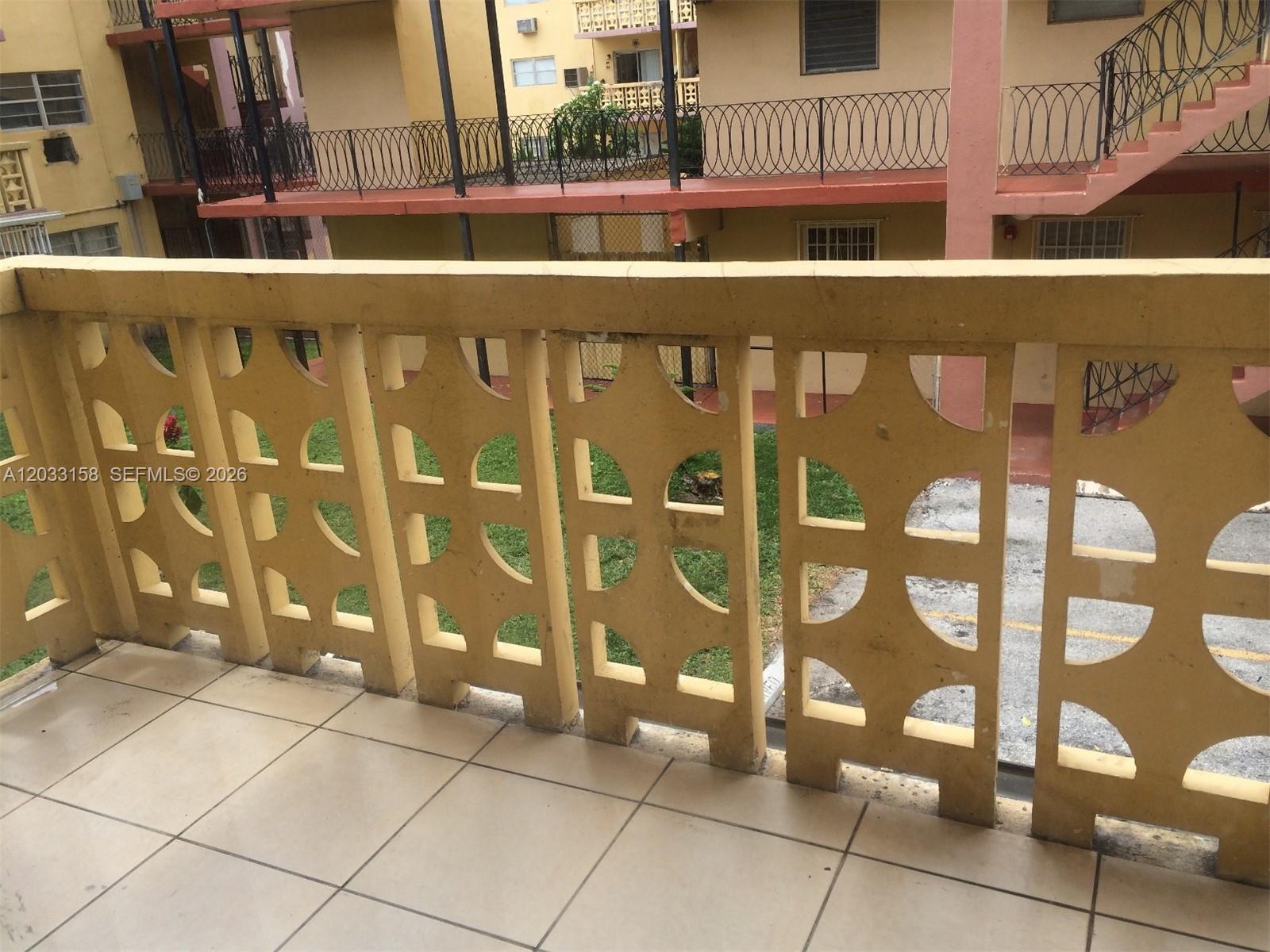 A balcony with a decorative concrete railing overlooks a courtyard and another apartment building — 2441 NW 13 ST # 77, Miami FL 33125, MIAMI, FL