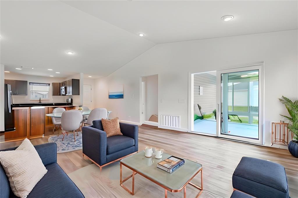 A bright living room with wood-look flooring opens to a kitchen and a screened patio — 7462 SAVANNA DRIVE, THE VILLAGES, FL