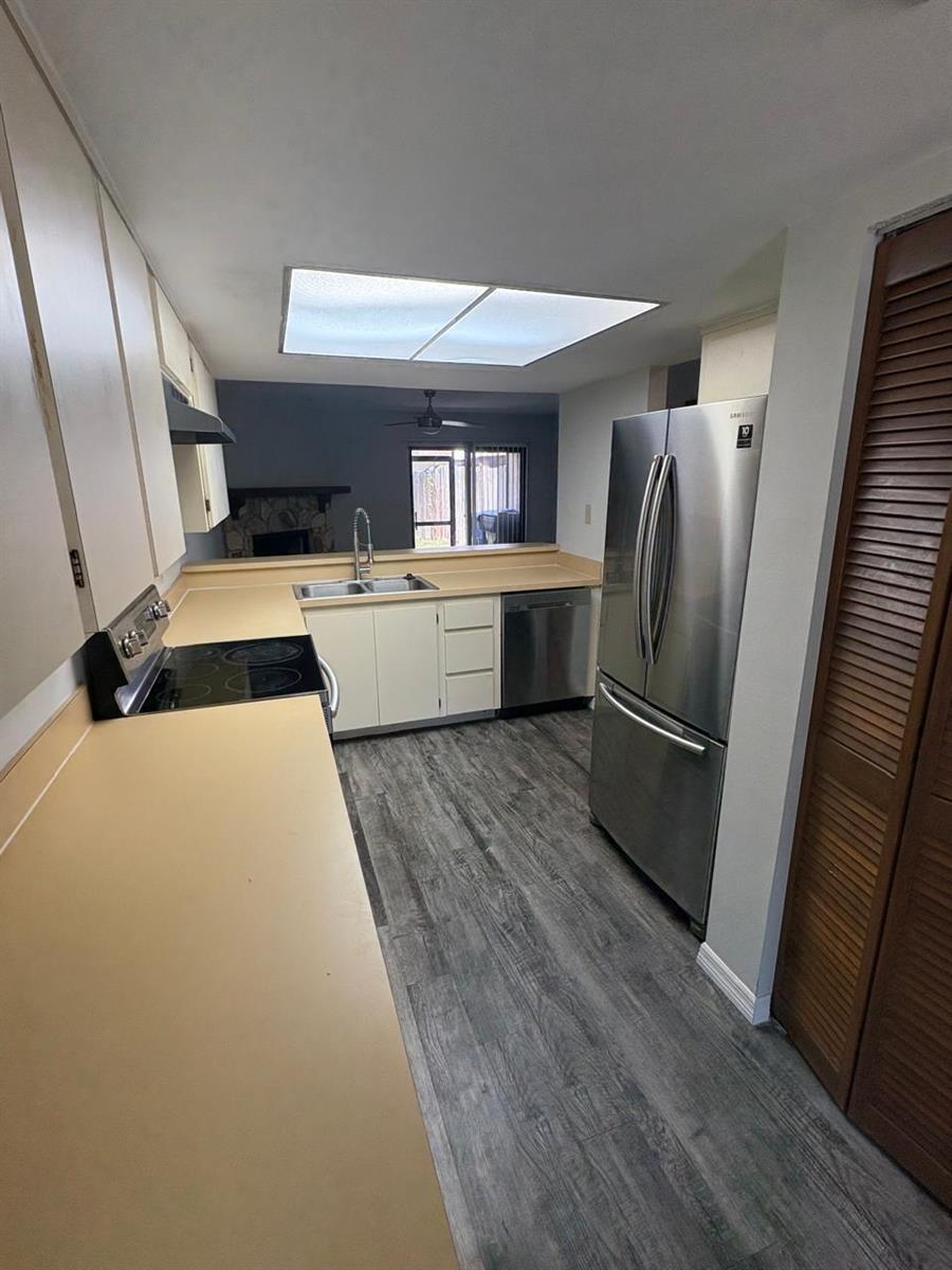 A kitchen with light-colored cabinets, tan countertops, stainless steel appliances, and gray wood-look flooring — 1838 Foxhall Circle, Kissimmee FL 34741, KISSIMMEE, FL