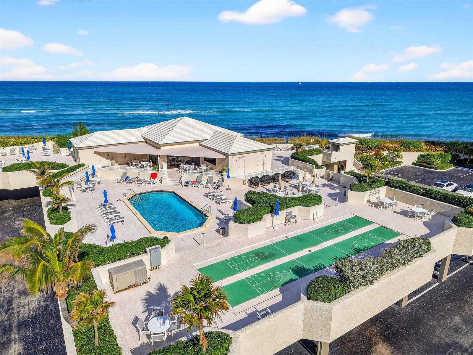 An aerial view shows a swimming pool, shuffleboard courts, and a clubhouse beside the ocean — 5540 N Ocean Drive # 1c, Singer Island FL 33404, SINGER ISLAND, FL