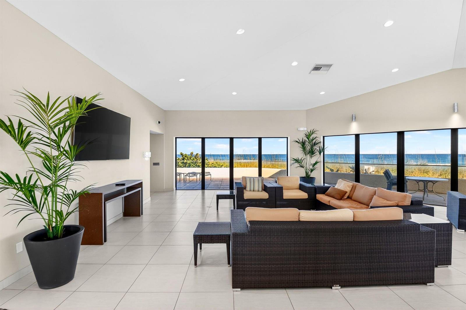 A spacious living room with tile floors, modern furniture, and large windows overlooking the ocean — 5540 N Ocean Drive # 1c, Singer Island FL 33404, SINGER ISLAND, FL