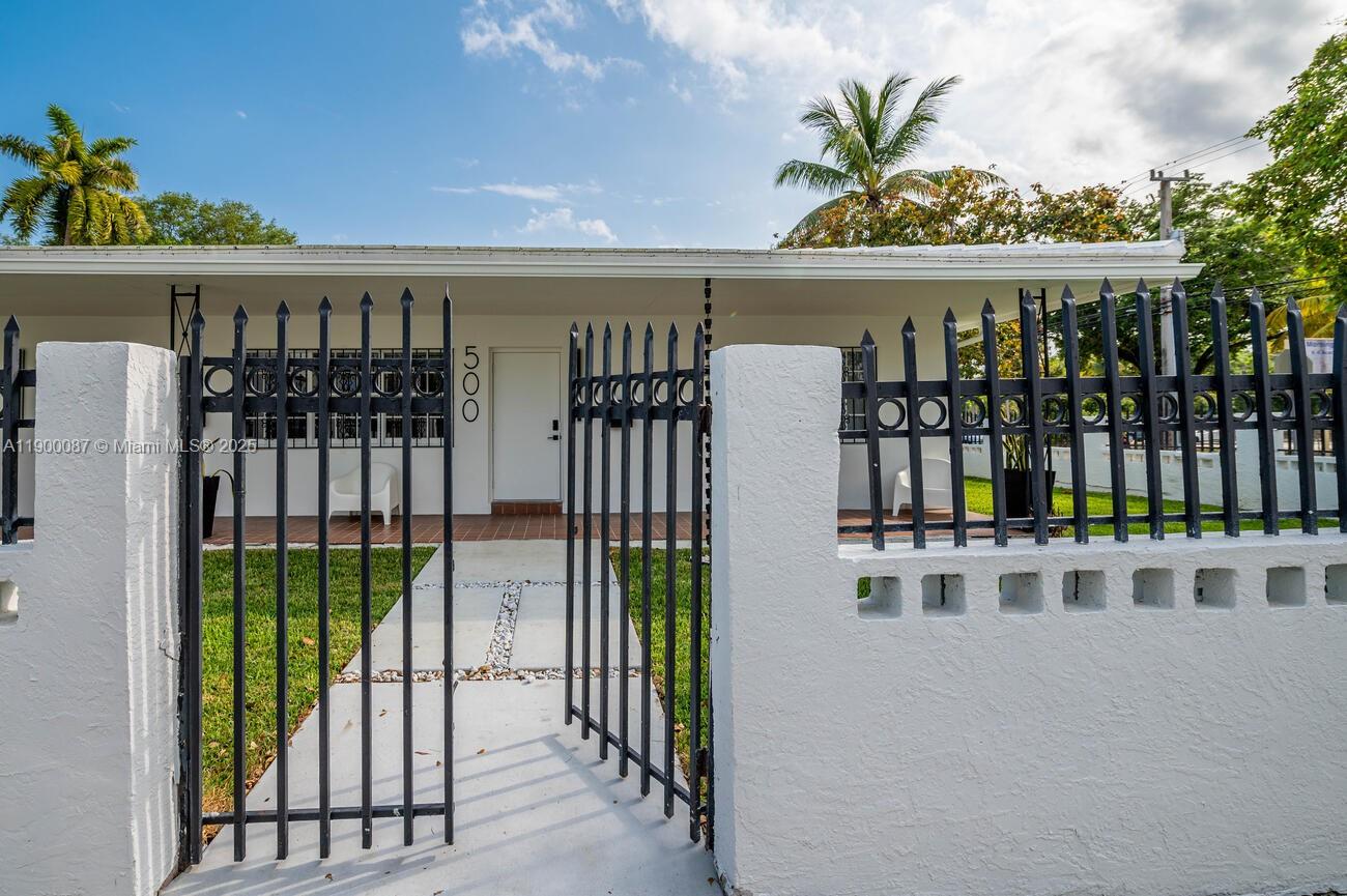 A white house with a black metal fence and gate stands behind a grassy yard — 510 NE 66th St # 1, Miami FL 33138, MIAMI, FL