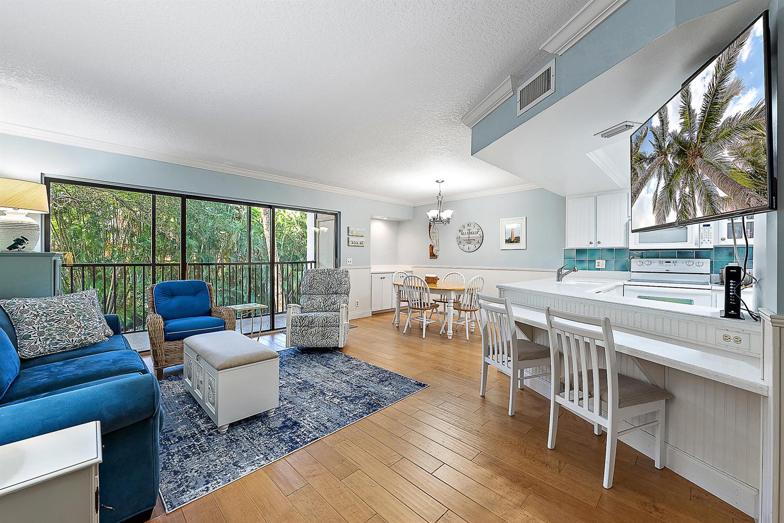 A living room and kitchen area with blue furniture, a patterned rug, and a balcony view — 1605 S Us Highway 1 # E204, Jupiter FL 33477, JUPITER, FL