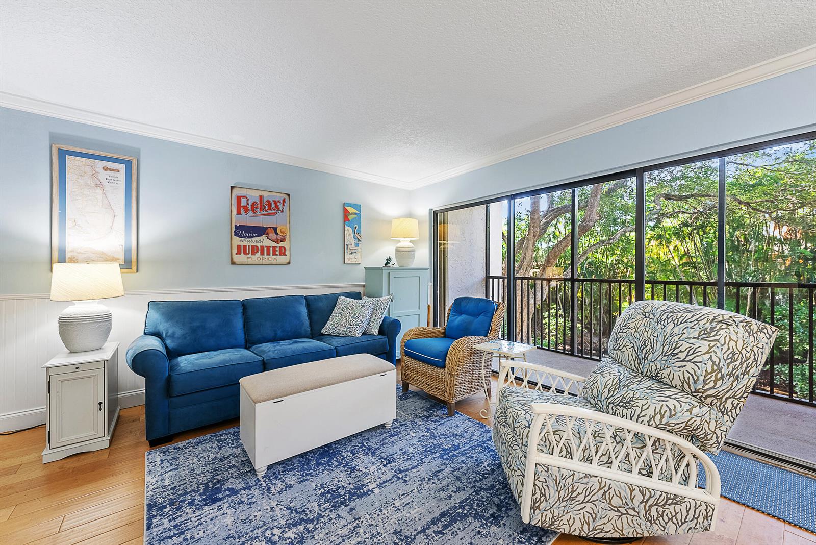 A living room features a blue sofa, patterned armchair, wicker chair, and a sliding glass door — 1605 S Us Highway 1 # E204, Jupiter FL 33477, JUPITER, FL