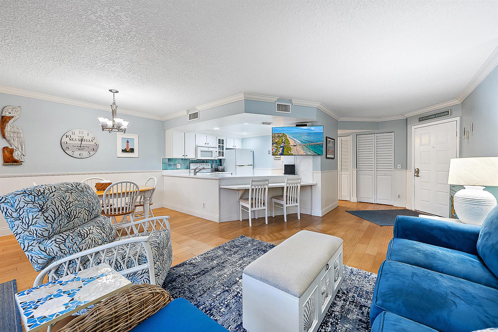 A bright living room and kitchen area features light blue walls, hardwood floors, and coastal decor — 1605 S Us Highway 1 # E204, Jupiter FL 33477, JUPITER, FL