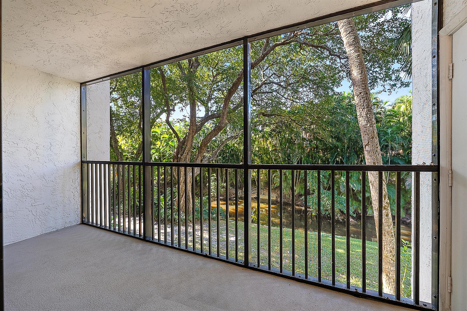 A screened-in balcony features a concrete floor, metal railings, and a view of trees — 1605 S Us Highway 1 # E204, Jupiter FL 33477, JUPITER, FL