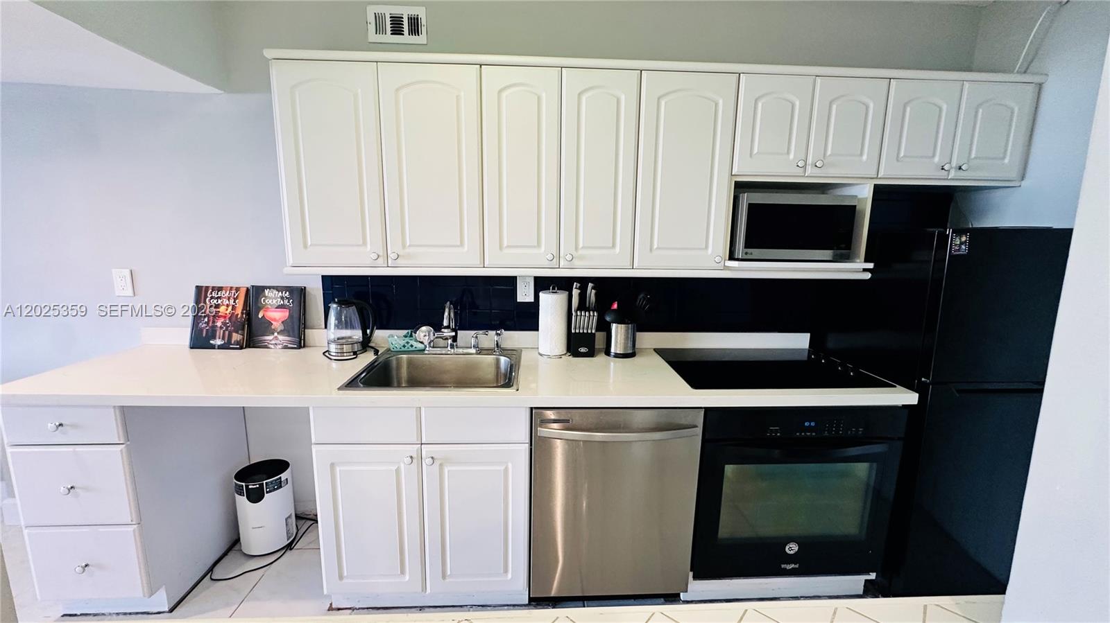 A kitchen features white cabinetry, stainless steel appliances, a black backsplash, and a white countertop — 100 Lincoln Rd # 720, Miami Beach FL 33139, MIAMI BEACH, FL