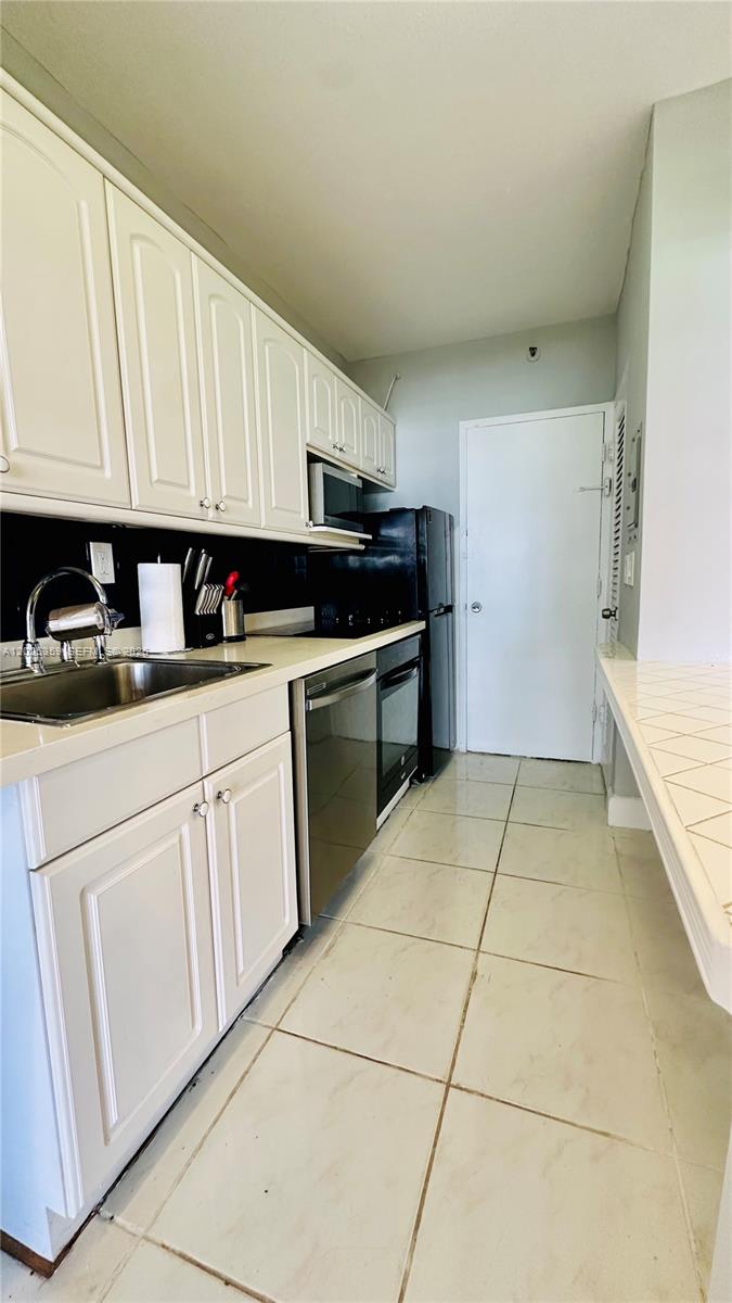 A galley kitchen features white cabinets, stainless steel appliances, and light-colored tile flooring — 100 Lincoln Rd # 720, Miami Beach FL 33139, MIAMI BEACH, FL
