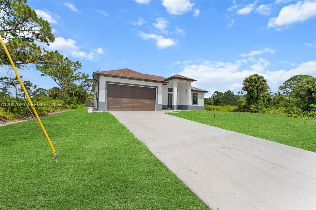 A single-story house with a brown garage door and a concrete driveway sits on grass — 1033 E Plymouth St E, Lehigh Acres FL 33974, LEHIGH ACRES, FL