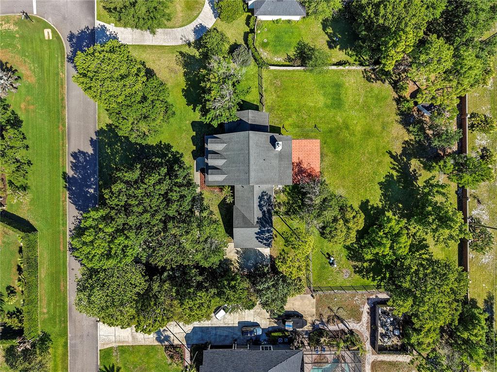 An aerial view shows a house with a dark roof surrounded by trees and grass — 761 N BELFAST PLACE, CHULUOTA, FL