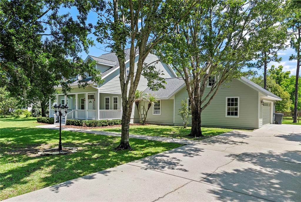 A two-story light green house with a front porch, attached garage, and surrounding trees — 761 N BELFAST PLACE, CHULUOTA, FL