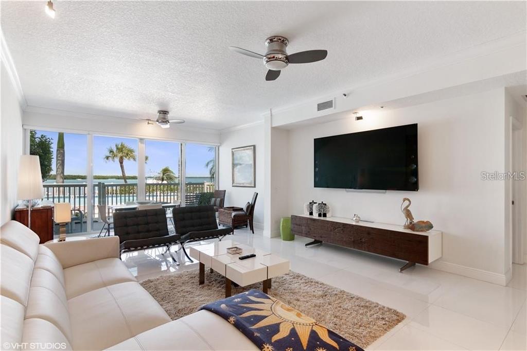 A living room features a white sofa, a large television, and sliding doors overlooking water — 615 DREAM ISLAND ROAD UNIT 107, LONGBOAT KEY, FL