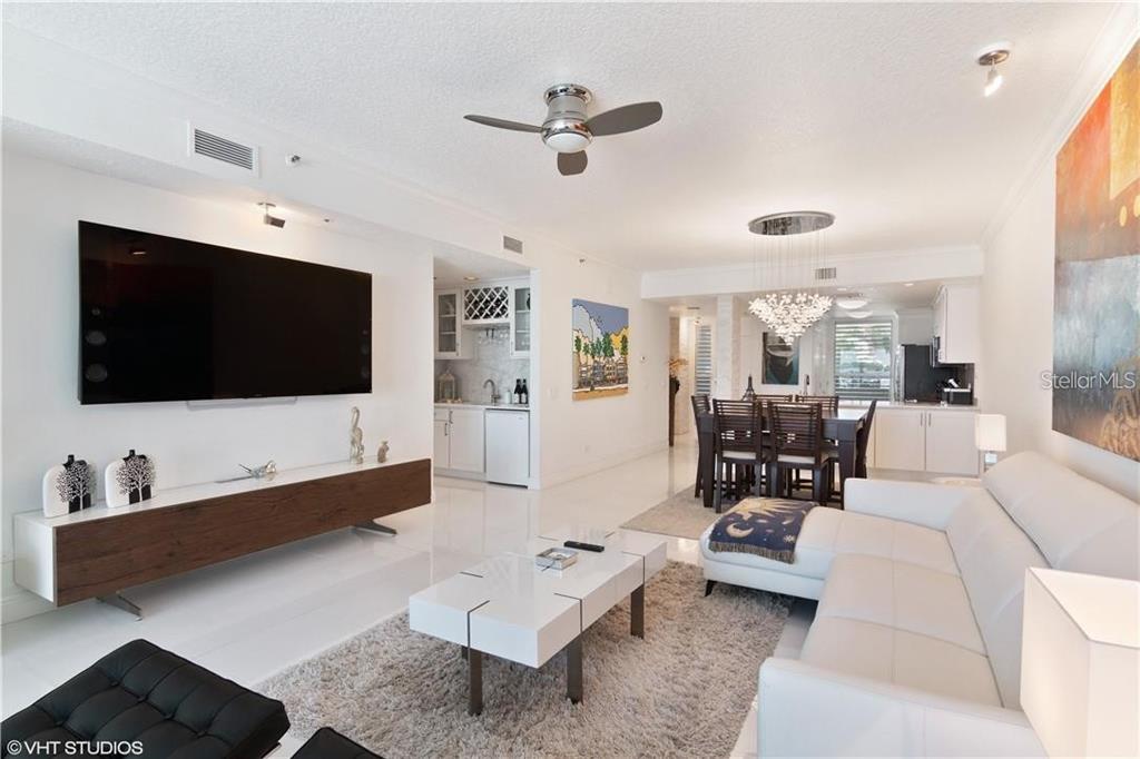 A modern living room features a white sofa, a television, and an adjacent dining area — 615 DREAM ISLAND ROAD UNIT 107, LONGBOAT KEY, FL