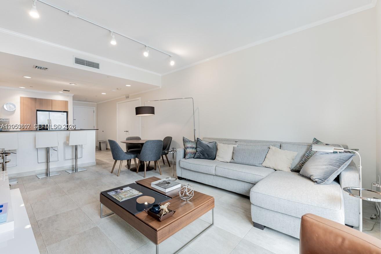 A modern living room features a gray sectional sofa, a wooden coffee table, and dining area — 1060 Brickell Ave # 1507, Miami FL 33131, MIAMI, FL