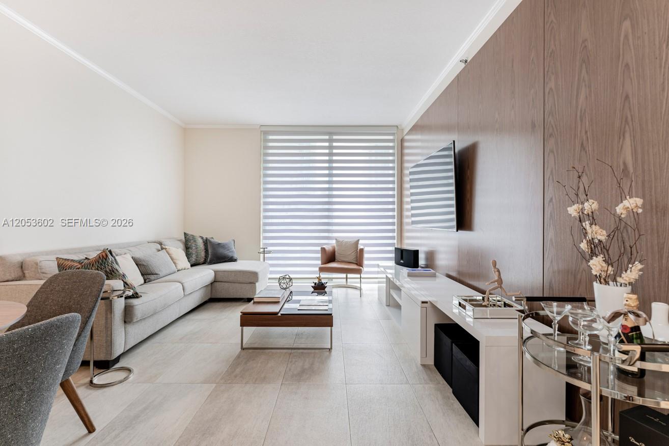 A modern living room features a grey sectional sofa, wood-paneled wall, and large window blinds — 1060 Brickell Ave # 1507, Miami FL 33131, MIAMI, FL