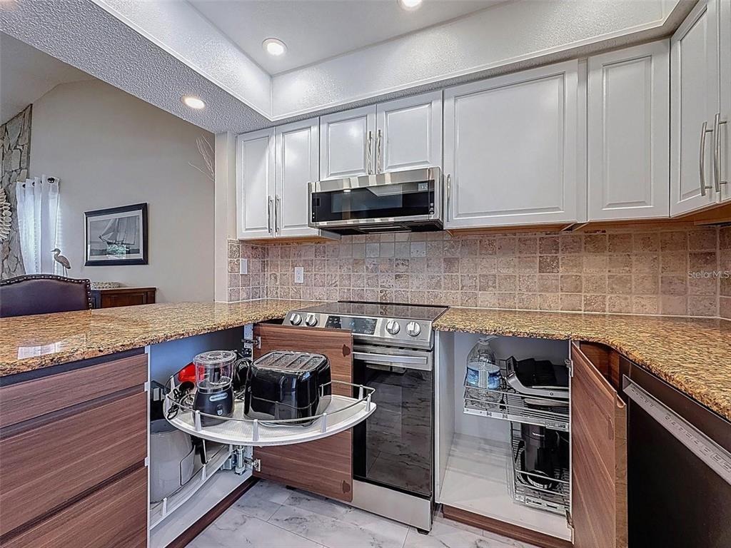 A kitchen features white upper cabinets, wood-tone lower cabinets, granite countertops, and stainless steel appliances — 9981 EAGLES PT CIRCLE UNIT 4, PORT RICHEY, FL