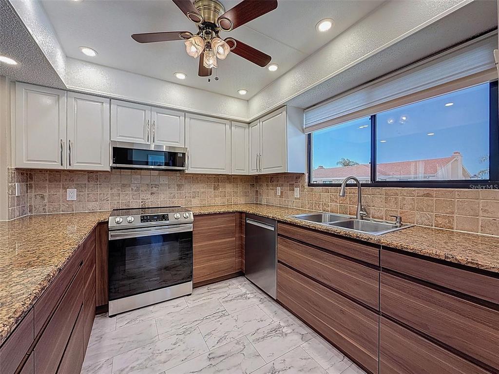 A kitchen features white upper cabinets, wood-tone lower cabinets, granite countertops, and stainless steel appliances — 9981 EAGLES PT CIRCLE UNIT 4, PORT RICHEY, FL