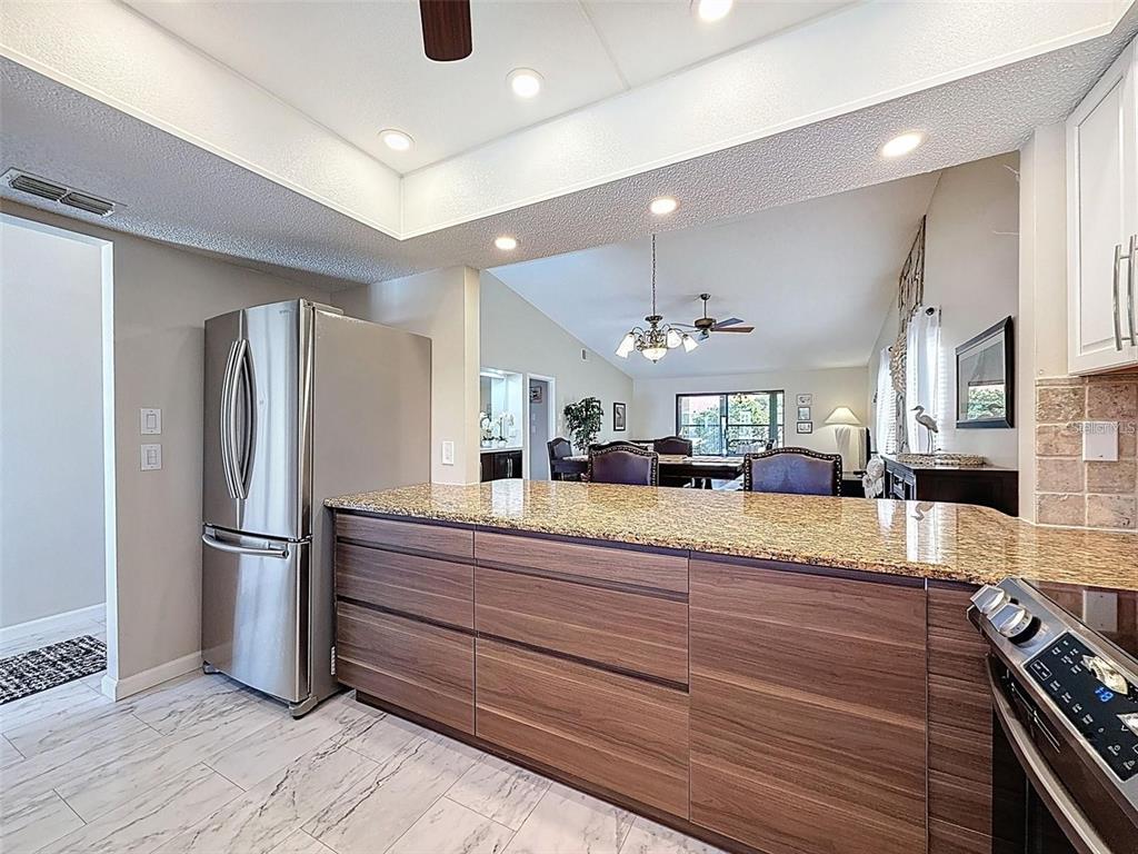 A kitchen with wood-grain cabinets, granite countertops, and stainless steel appliances overlooks a dining area — 9981 EAGLES PT CIRCLE UNIT 4, PORT RICHEY, FL