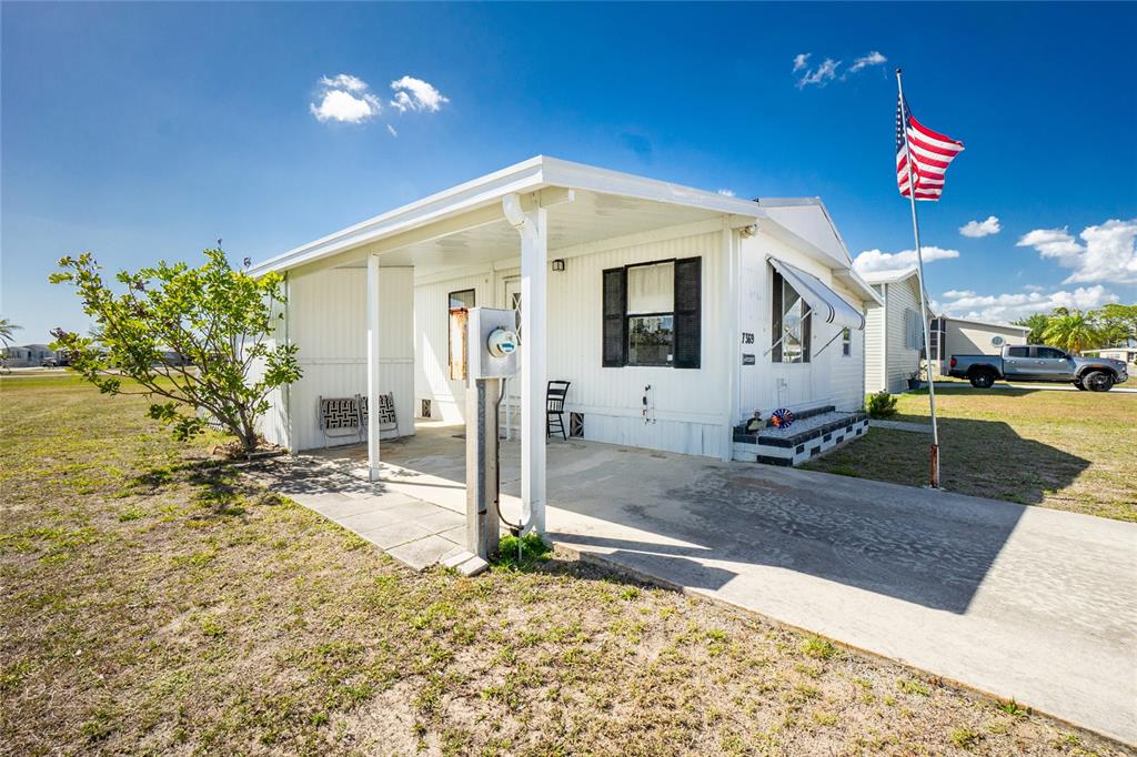 A white mobile home with a carport, concrete driveway, and an American flag — 7369 CANDACE LANE, PORT CHARLOTTE, FL