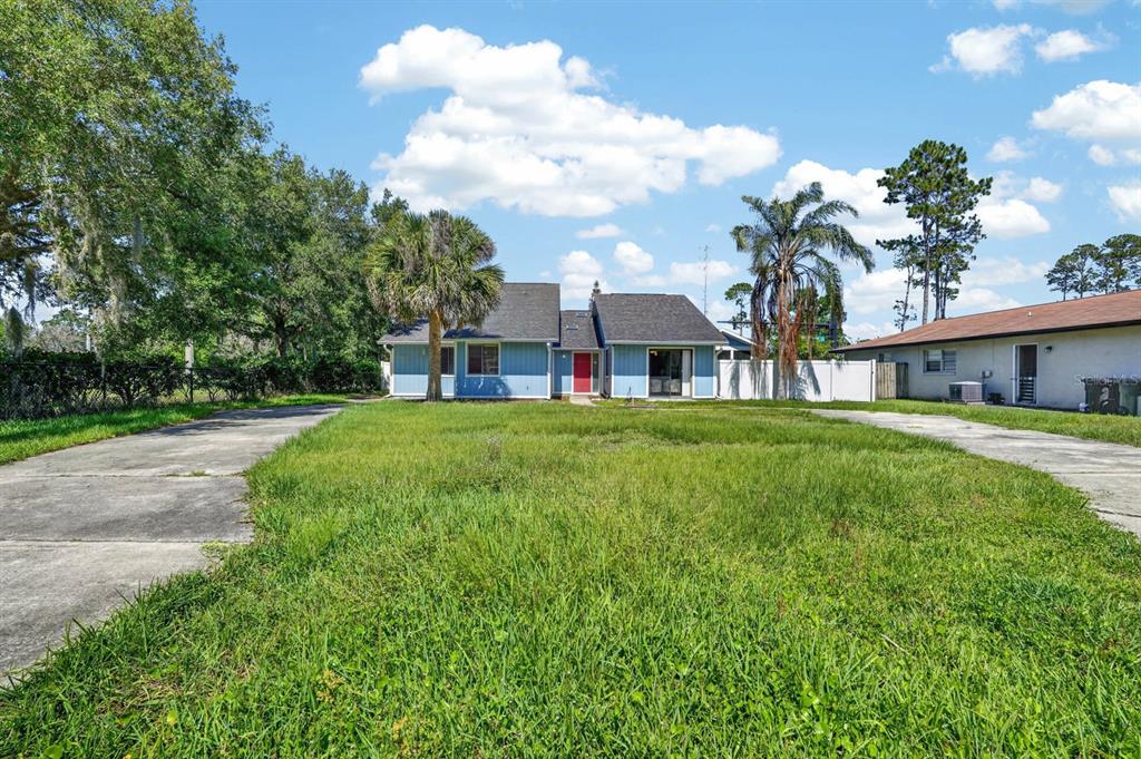 A blue single-story house with a red front door sits behind a large grassy yard — 58 BRADMORE LANE UNIT A, PALM COAST, FL