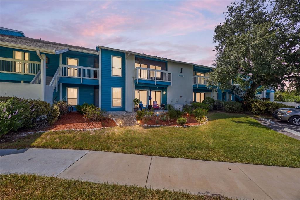 A two-story blue apartment building with white railings and a landscaped front yard at sunset — 455 ALT 19 S UNIT 159, PALM HARBOR, FL