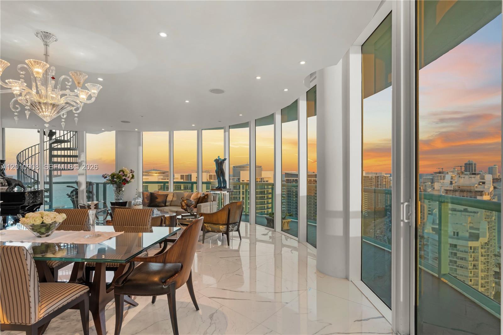 A dining area with a glass table and marble floors overlooks a city sunset view — 6000 Indian Creek Dr # 3, Miami Beach FL 33140, MIAMI BEACH, FL