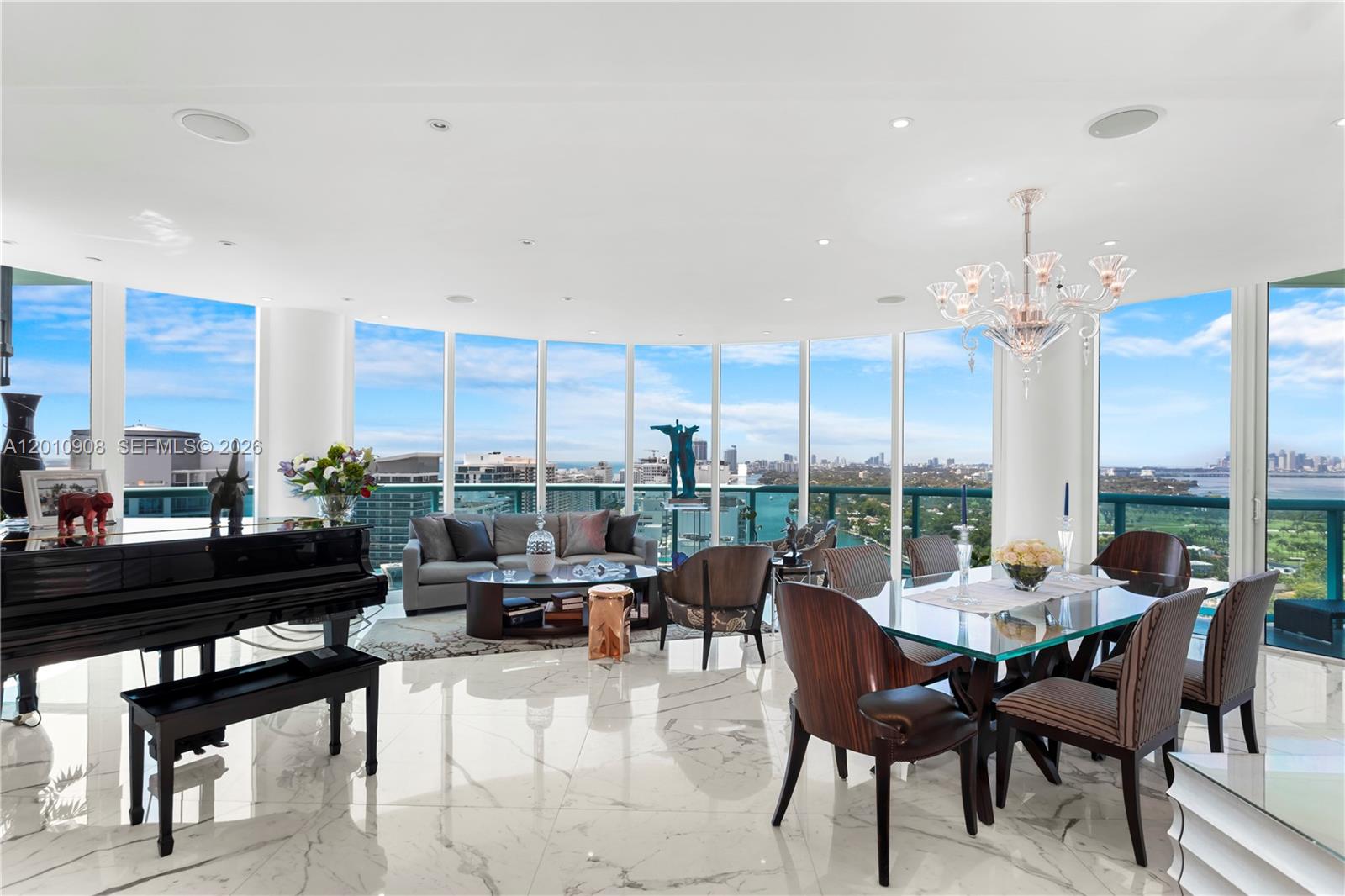 A bright living and dining area features floor-to-ceiling windows, marble floors, and a grand piano — 6000 Indian Creek Dr # 3, Miami Beach FL 33140, MIAMI BEACH, FL
