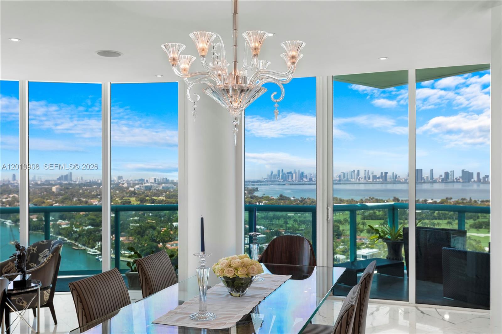 A dining room with a glass table, crystal chandelier, and floor-to-ceiling windows overlooking a city — 6000 Indian Creek Dr # 3, Miami Beach FL 33140, MIAMI BEACH, FL