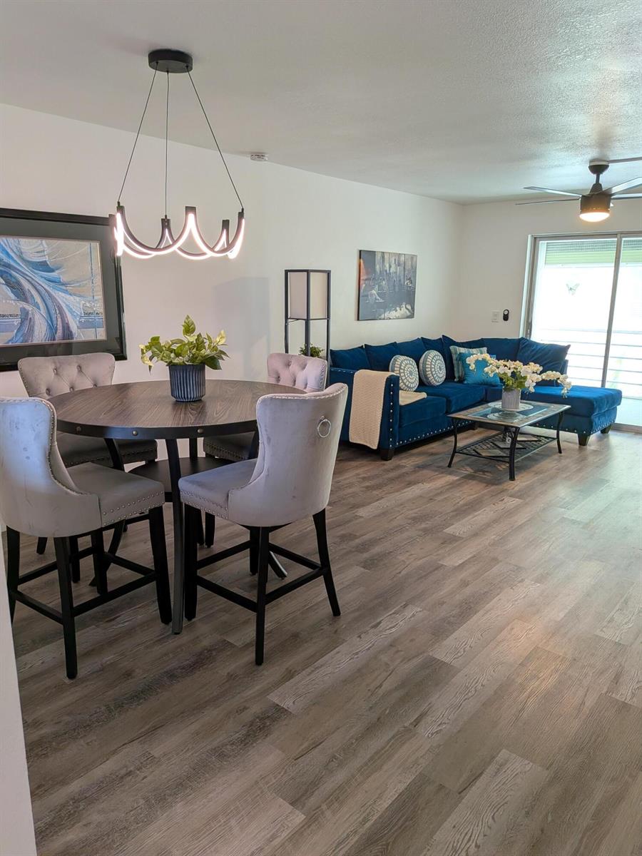 An open-concept living and dining area features wood-look flooring, a blue sectional, and round table — 2601 NE 3rd Court # 2100, Boynton Beach FL 33435, BOYNTON BEACH, FL