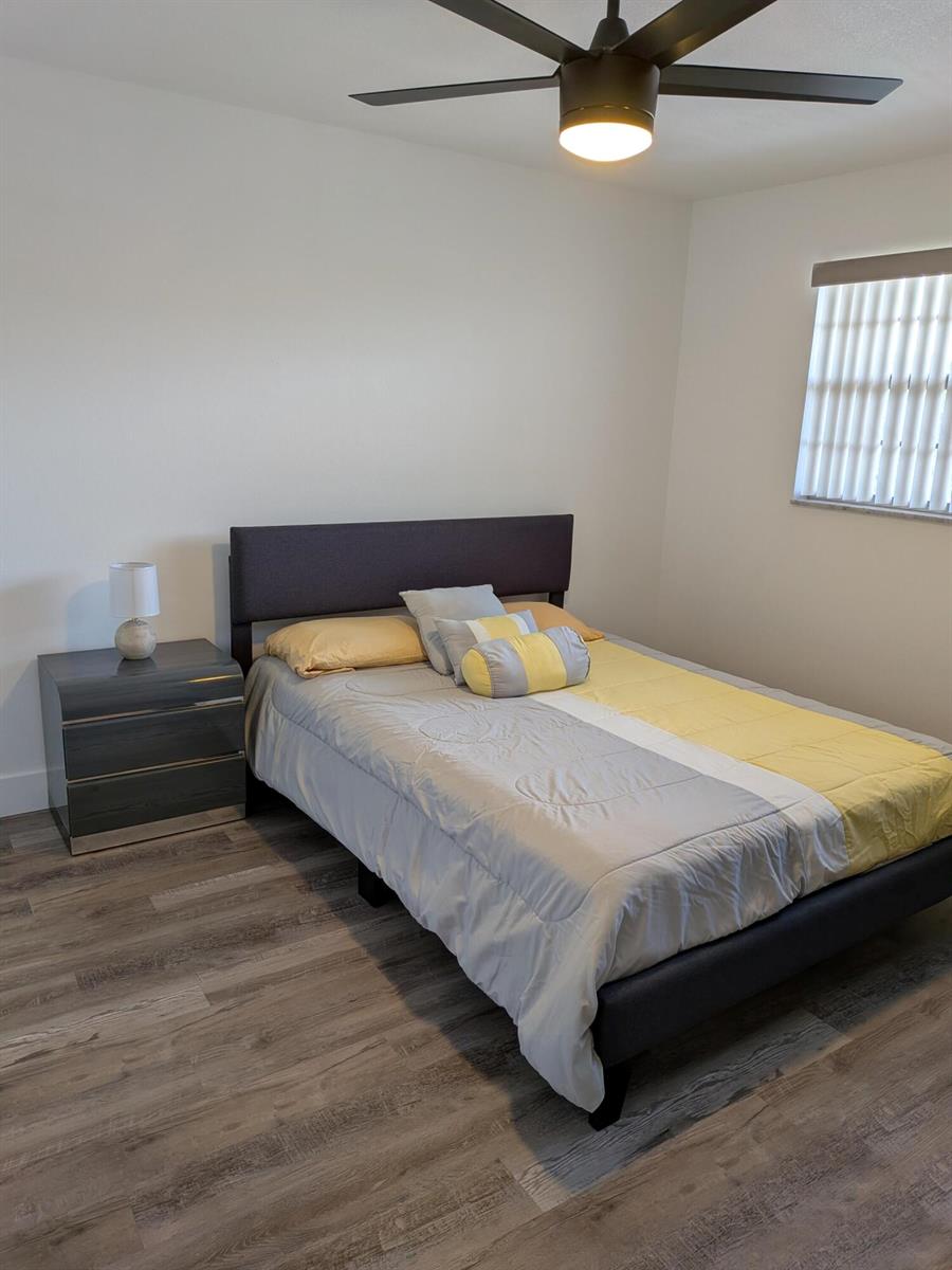 A bedroom features a gray upholstered bed, a matching nightstand, and wood-look flooring — 2601 NE 3rd Court # 2100, Boynton Beach FL 33435, BOYNTON BEACH, FL