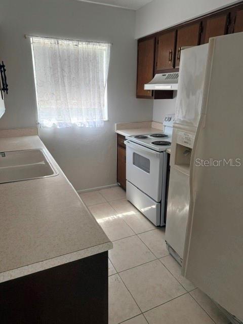 A kitchen features white appliances, wood cabinets, a window with a curtain, and tiled floors — 1100 E CAROLINE STREET UNIT 119, TAVARES, FL