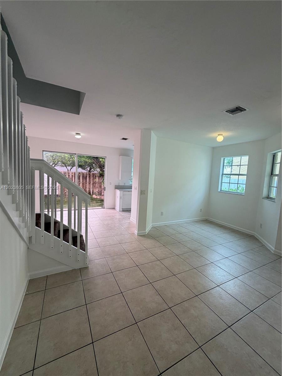An open-concept living area features tile flooring, a white staircase, and a sliding glass door — 607 NE 21st Ter, Homestead FL 33033, HOMESTEAD, FL