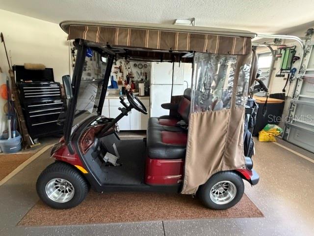 A red and black golf cart with a tan canopy is parked inside a garage — 1448 GABLE PLACE, THE VILLAGES, FL