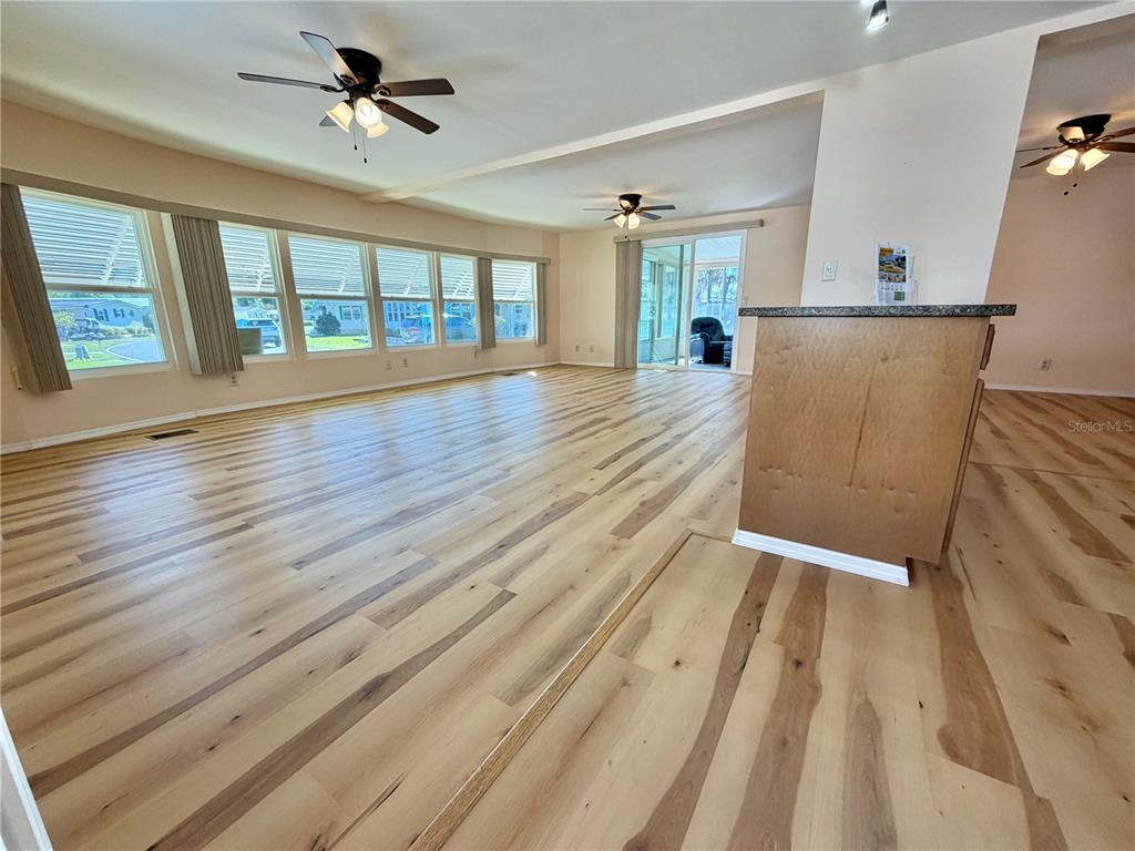 A spacious living area features light wood-look flooring, multiple ceiling fans, and large windows — 176 AZALEA TRAIL, LEESBURG, FL