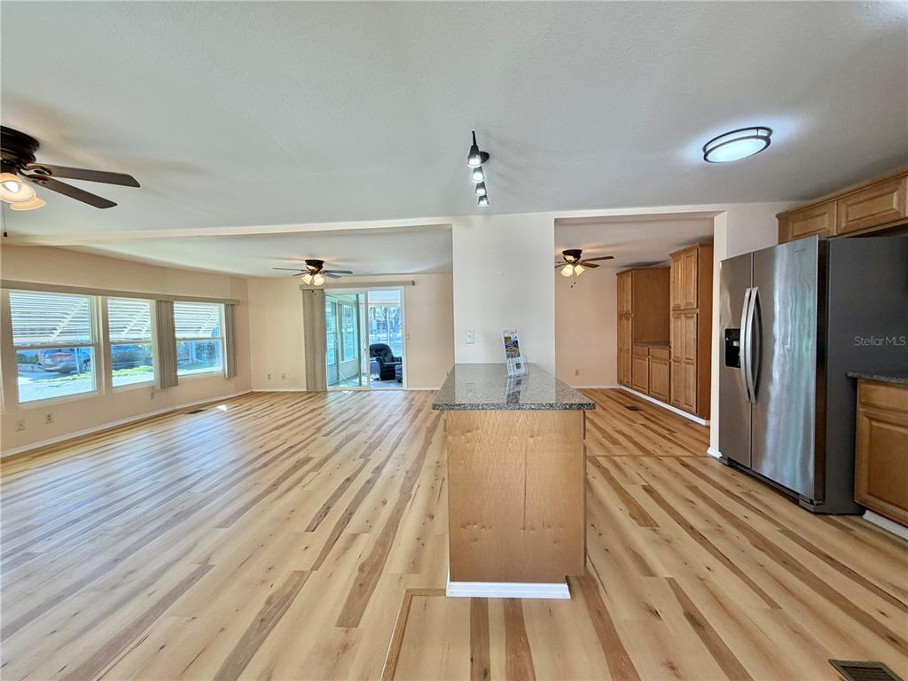 An open-concept kitchen and living area features light wood flooring, a granite-topped island, and stainless-steel appliances — 176 AZALEA TRAIL, LEESBURG, FL
