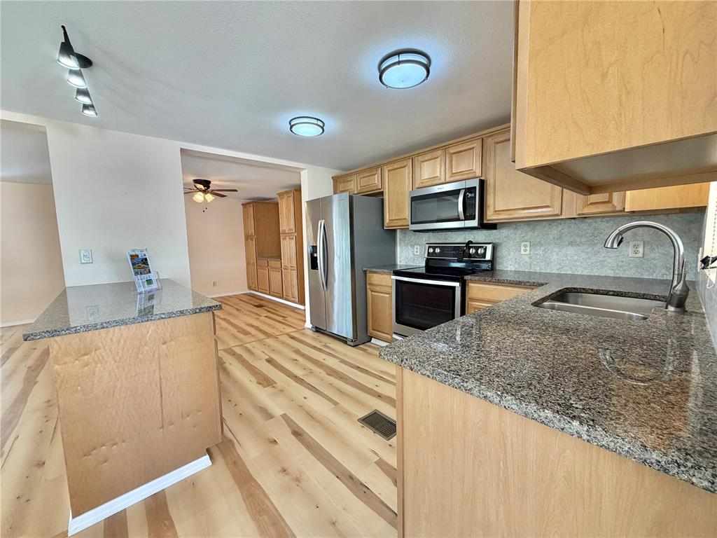 A kitchen features light wood cabinets, granite countertops, stainless steel appliances, and light wood flooring — 176 AZALEA TRAIL, LEESBURG, FL
