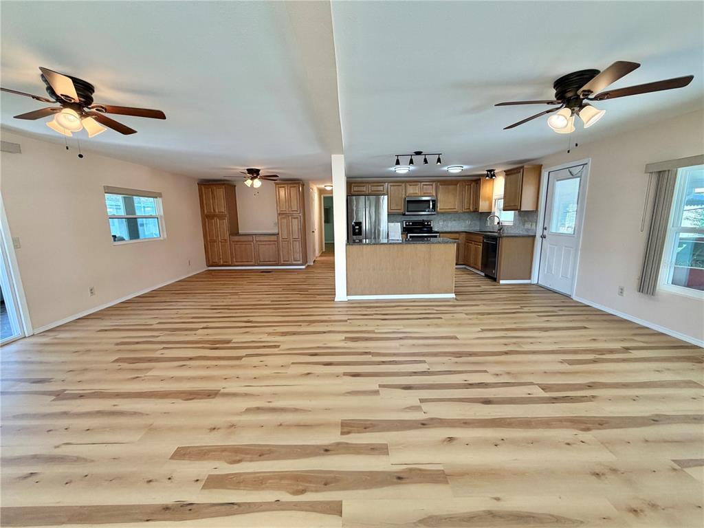 An open-concept living area features light wood-look flooring, a kitchen with wooden cabinets, and ceiling fans — 176 AZALEA TRAIL, LEESBURG, FL