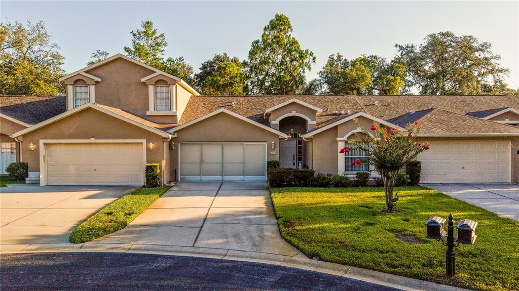 A tan suburban house with three garage doors, a front entrance, and a grassy lawn — 7541 MOORGATE COURT, NEW PORT RICHEY, FL